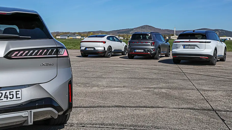 Vergleichstest BMW iX3, Polestar 4, Nio EL6 und Smart #5 BMW iX3, Polestar 4, Nio EL6 und Smart #5 stehen nebeneinander auf einer breiten Asphaltstrecke. Ein silberner BMW steht im Vordergrund unter blauem Himmel.