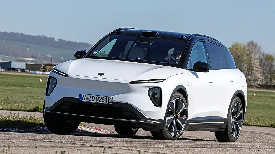 Vergleichstest BMW iX3, Polestar 4, Nio EL6 und Smart #5 Ein weißer Nio EL6 fährt auf einer asphaltierten Strecke. Im Hintergrund liegen Wiesen und Bäume.