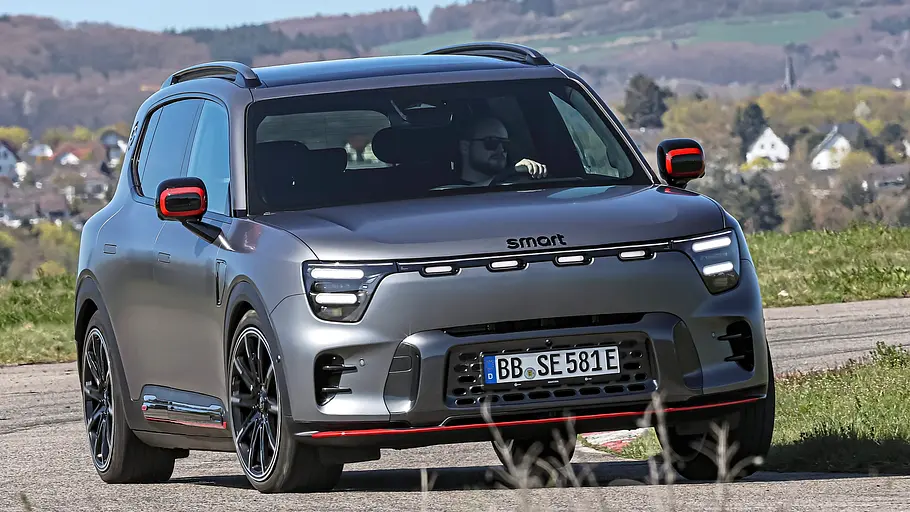 Vergleichstest BMW iX3, Polestar 4, Nio EL6 und Smart #5 Ein grauer Smart #5 fährt auf einer asphaltierten Strecke. Im Hintergrund liegen Wiesen und Bäume.