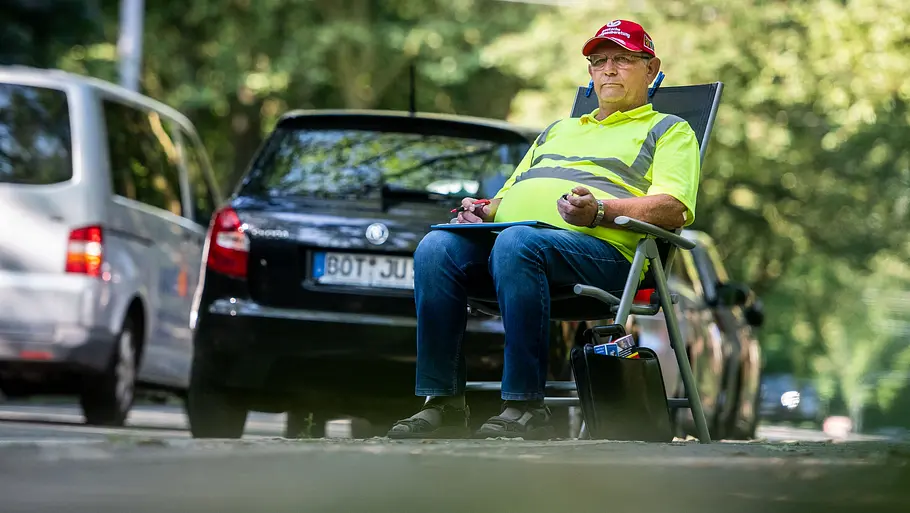 Ein Mann mit Zählgerät und Clipboad sitzt in einem Klappstuhl und erfasst den vorbeifließenden Verkehr.