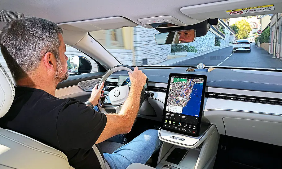 Blick aus dem Fond aus in das Cockpit: Jemand sitzt am Steuer des Volvo ES90 (2025).