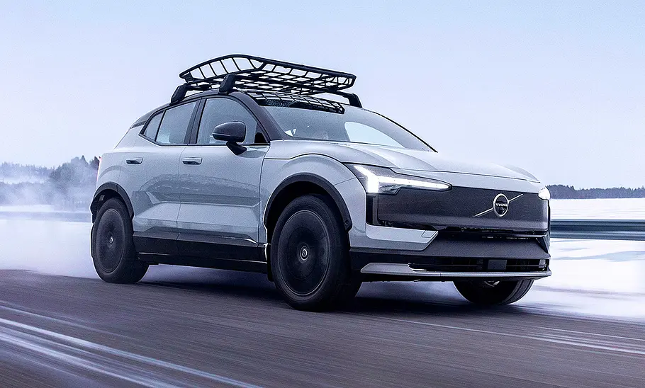 Blick von schräg vorne auf den in einer Schneelandschaft fahrenden Volvo EX30 Cross Country (2025).