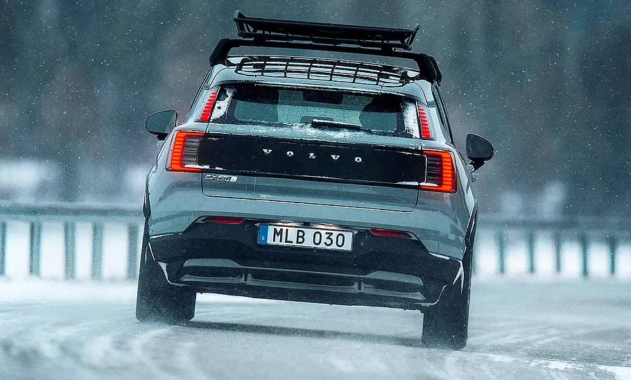 Blick von hinten auf den in einer Schneelandschaft fahrenden Volvo EX30 Cross Country (2025).
