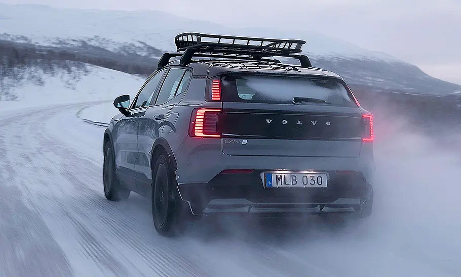 Blick von schräg hinten auf den in einer Schneelandschaft fahrenden Volvo EX30 Cross Country (2025).