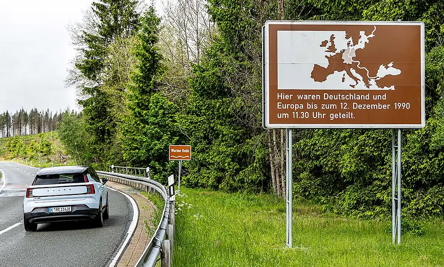 Der Volvo EX30 Single Motor Extended Range Ultra fährt durch den Harz, vorbei am Schild zur deutsch-deutschen-Grenze, fotografiert von hinten.
