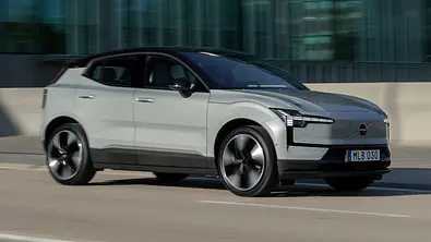 Der Volvo EX30 fahrend von schräg vorne rechts auf einer Straße in städtischem Umfeld. - Foto: Volvo