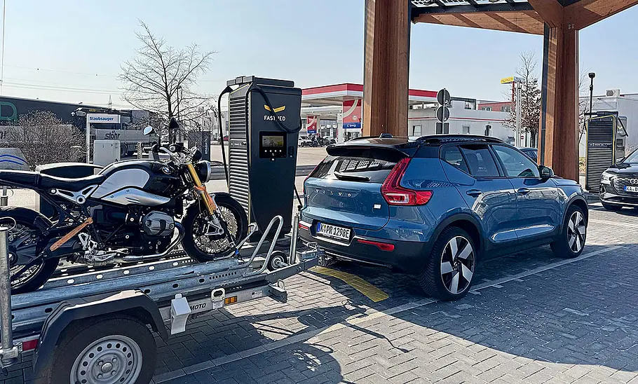 Der Volvo XC40 Recharge Extended Range mit Motorradanhänger an einer Ladestation, fotografiert von schräg hinten.