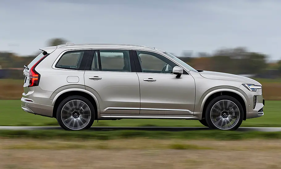 Das Volvo XC90 Facelift (2024) fährt über eine Landstraße, von der Seite fotografiert.