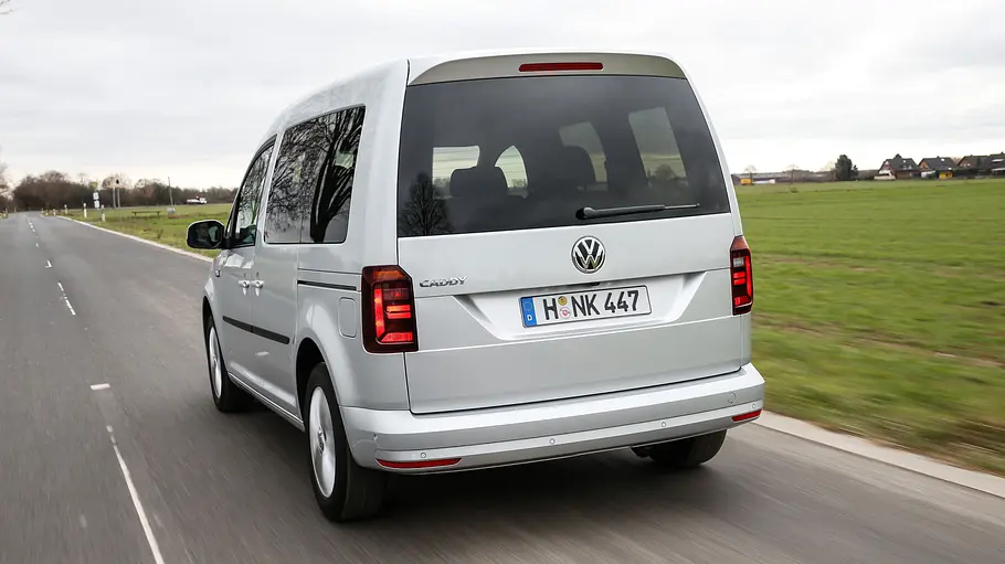 Der VW Caddy (2015) fährt auf einer Landstraße, von hinten links fotografiert.