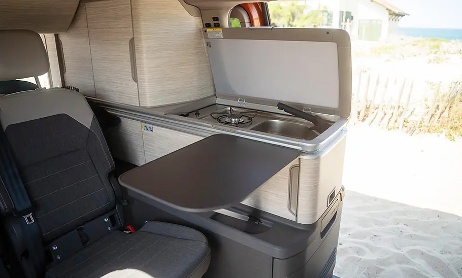 VW California 1.5 eHybrid 4Motion (2025) Die Innenaufnahme zeigt die Küchenzeile des VW California 1.5 eHybrid 4Motion (2025).