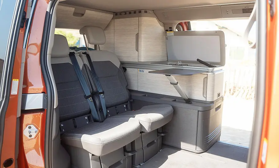 VW California 1.5 eHybrid 4Motion (2025) Das von außen bei geöffneter Seitentür aufgenommene Foto zeigt die Rückbank des VW California 1.5 eHybrid 4Motion (2025).