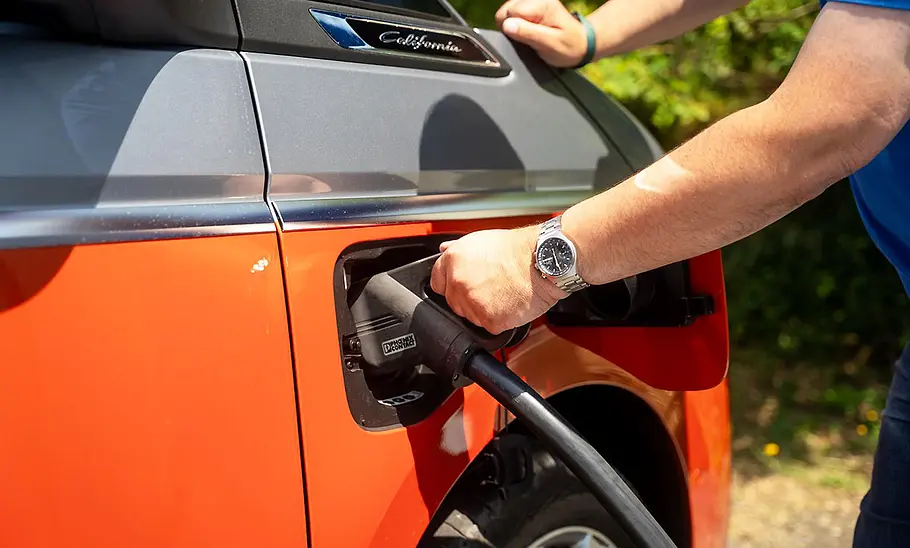 VW California 1.5 eHybrid 4Motion (2025) Die Außenaufnahme zeigt die Hand eines Testers beim Anstöpseln des Ladekabels.