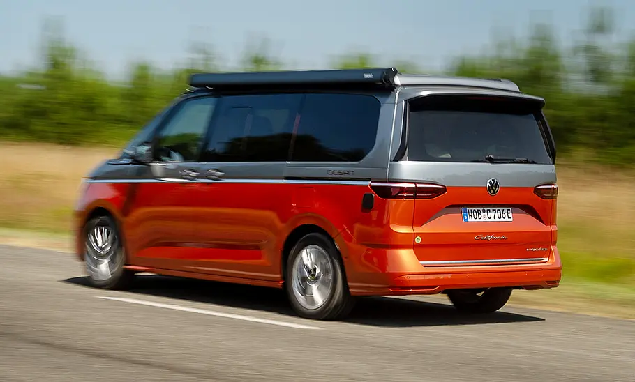 VW California 1.5 eHybrid 4Motion (2025) Die fahrdynamische Aufnahme zeigt den VW California 1.5 eHybrid 4Motion (2025) von schräg hinten.