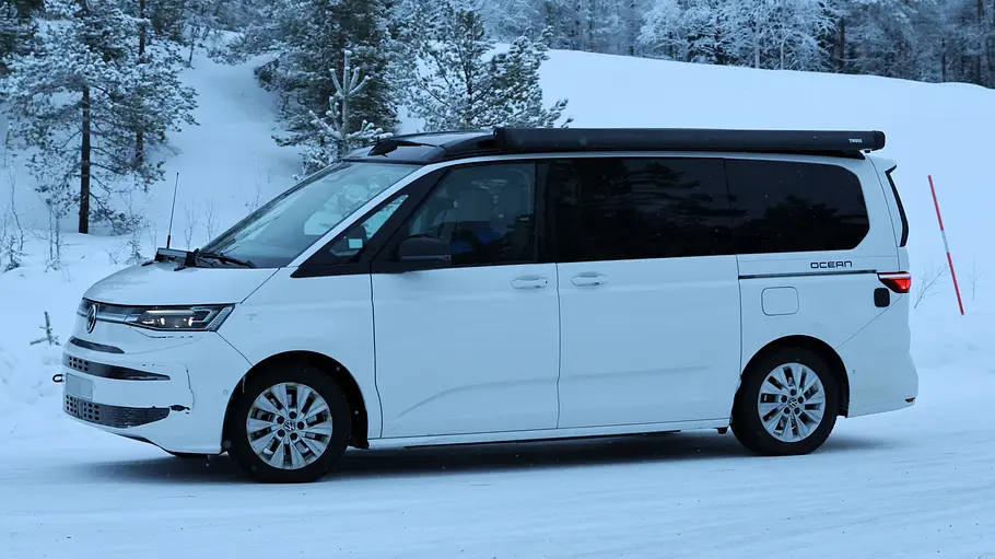 Ein Erlkönig des VW California Facelift auf einer Erprobungsfahrt in Nordschweden auf verschneiter Straße von schräg vorne links.