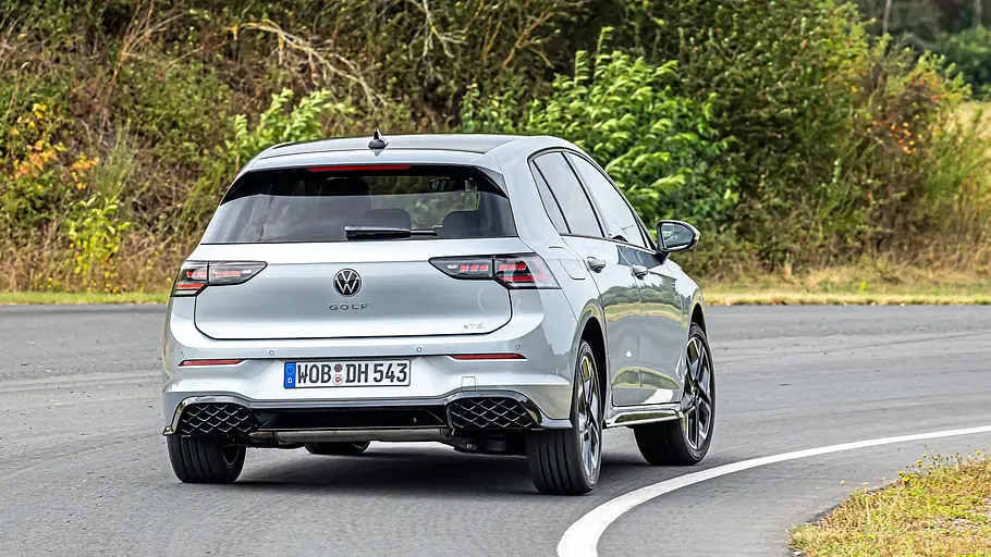 Ein silberner VW Golf ist von schräg hinten auf einer asphaltierten Kurve zu sehen. Büsche und Bäume säumen die Straße.