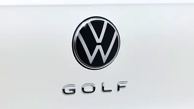 Eine Detailaufnahme zeigt ein VW-Emblem und einen Golf-Schriftzug am Heck eines Autos - Foto: VW