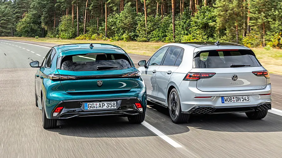 Ein türkisfarbener Peugeot 308 und ein silberner VW Golf fahren nebeneinander auf einer Straße am Wald, von hinten gesehen.