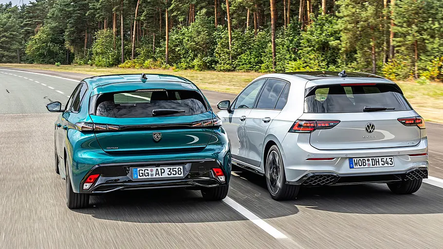 Ein silberner VW Golf R-Line und ein türkisfarbener Peugeot 308 fahren nebeneinander auf einer Landstraße mit Bäumen im Hintergrund..
