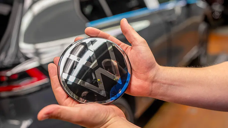 Eine Person in einem VW-Werk hält das Markenemblem in beiden Händen.