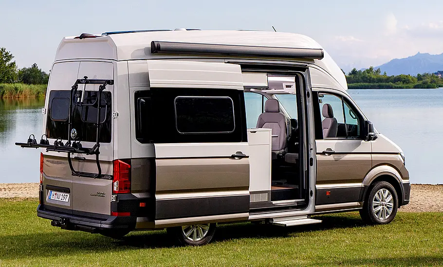 VW Grand California (2018) Der VW Grand California (2018) stehend von schräg hinten fotografiert, mit offener Schiebetür.