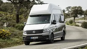Das VW Grand California Facelift von schräg vorne links zu sehen fährt durch eine Rechtskurve auf einer spanischen Landstraße. - Foto: VW Nutzfahrzeuge/Ingo Barenschee