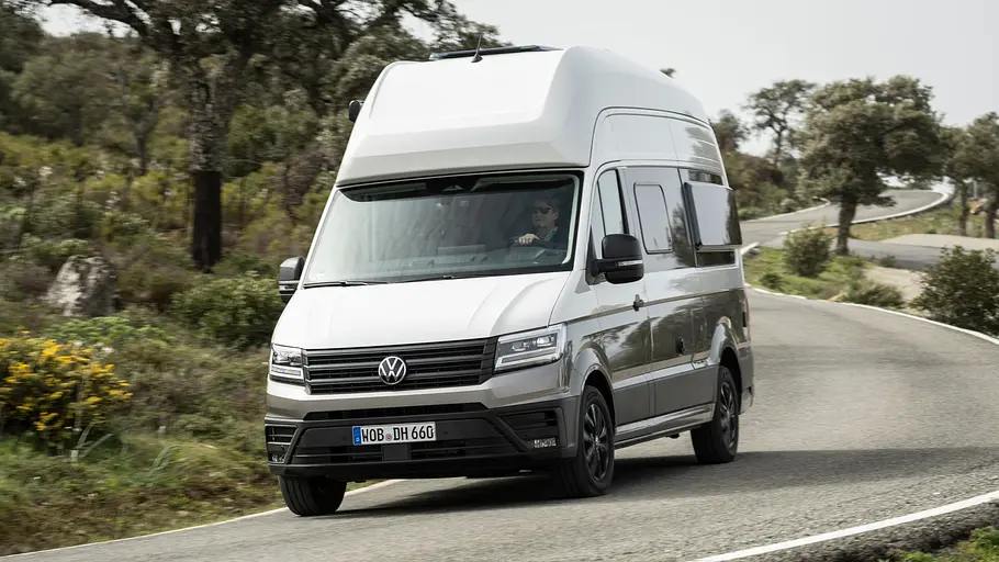 VW Grand California Facelift Fahrbericht Das VW Grand California Facelift von schräg vorne links zu sehen fährt durch eine Rechtskurve auf einer spanischen Landstraße.
