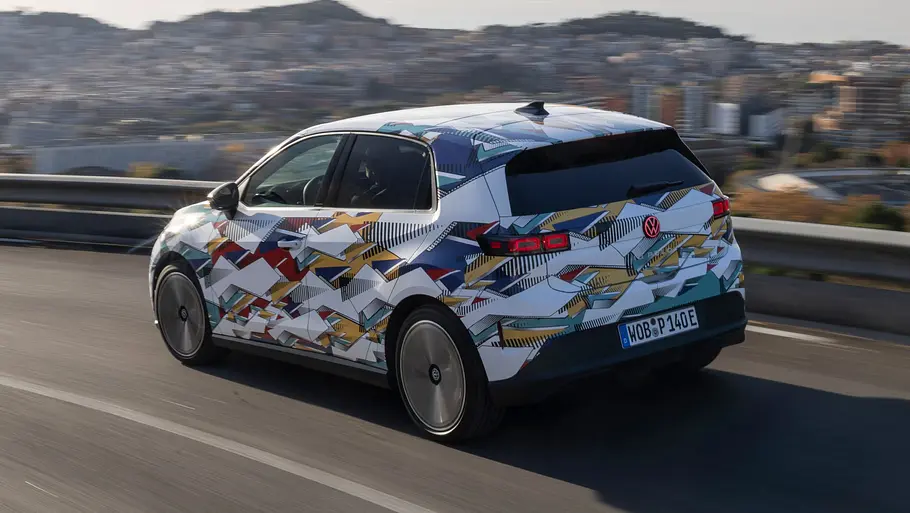 VW ID. Polo (2026) Der VW ID. Polo fährt als getarnter Prototyp über eine Landstraße, von hinten links fotografiert.