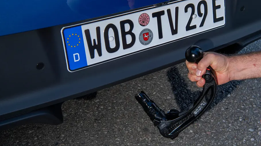 VW ID. Polo Fahrbericht Eine Hand hält die abnehmbare Anhängerkupplung des VW ID. Polo an die Aufnahme unter dem hinteren Stoßfänger.