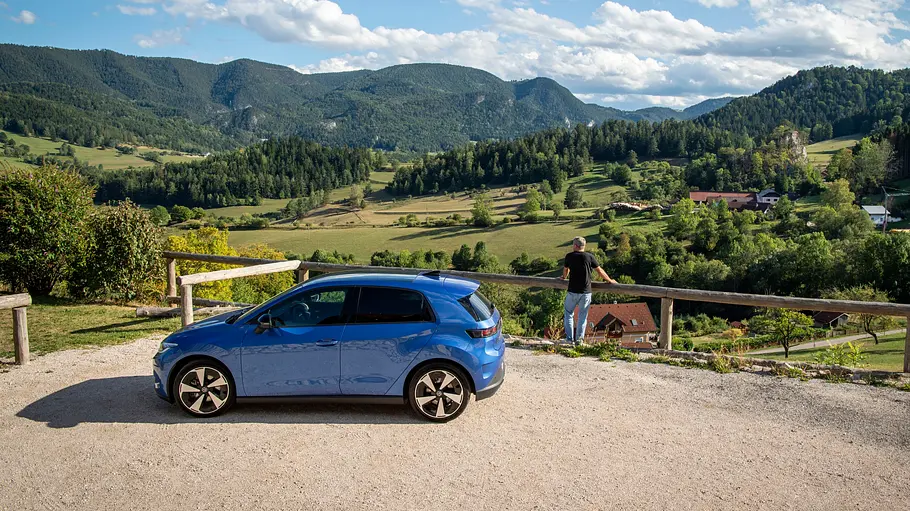 VW ID. Polo Fahrbericht Der VW ID. Polo statisch auf einem Schotterparkplatz an einem Aussichtspunkt. Eine Person lehnt sich neben dem Auto an eine Holzreling.