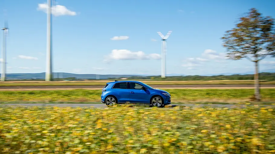 VW ID. Polo Fahrbericht Der VW ID. Polo fährt an Windrädern vorbei, fotografiert von der Seite rechts.