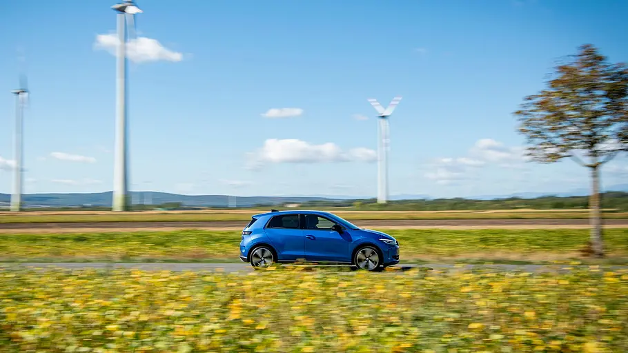 VW ID. Polo Fahrbericht Der VW ID. Polo fährt an Windrädern vorbei, fotografiert von der Seite rechts.