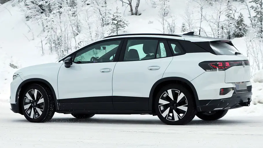 VW ID.4/ID. Tiguan Der VW ID.4 fährt als Erlkönig durch den Schnee, fotografiert von schräg hinten.