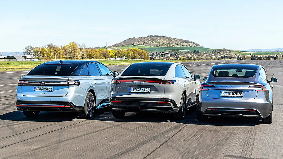 Blick von schräg hinten auf die drei fahrenden Elektro-Limousinen VW ID.7, Mazda6e und Tesla Model 3.