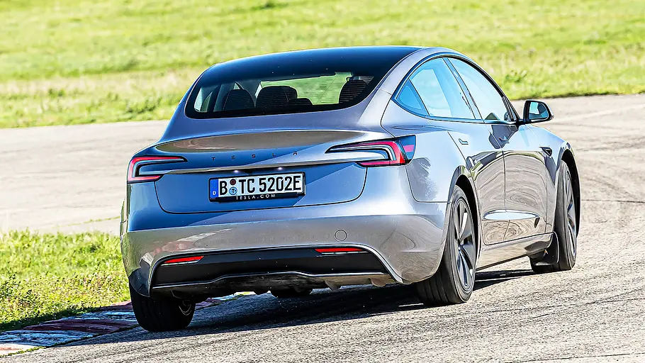 Blick von schräg hinten auf den fahrenden Tesla Model 3.