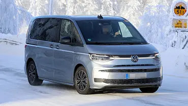 Das VW Multivan Facelift (2026) fährt als Erlkönig auf einer verschneiten Straße, von vorne rechts fotografiert. - Foto: SH Proshots Das VW Multivan Facelift (2026) fährt als Erlkönig auf einer verschneiten Straße, von vorne rechts fotografiert. - Foto: SH Proshots