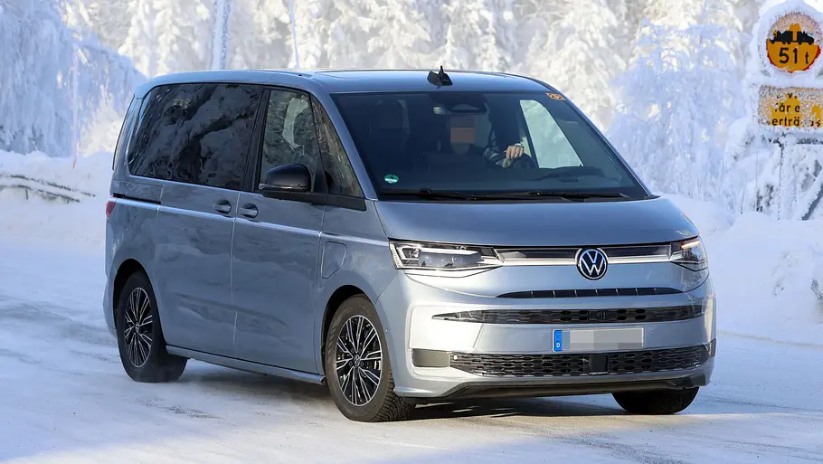 Das VW Multivan Facelift (2026) fährt als Erlkönig auf einer verschneiten Straße, von vorne rechts fotografiert.