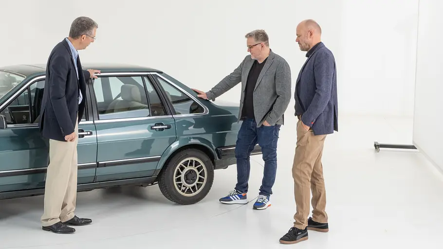 Drei Personen am Heck des VW Santana stehend fotografiert. 