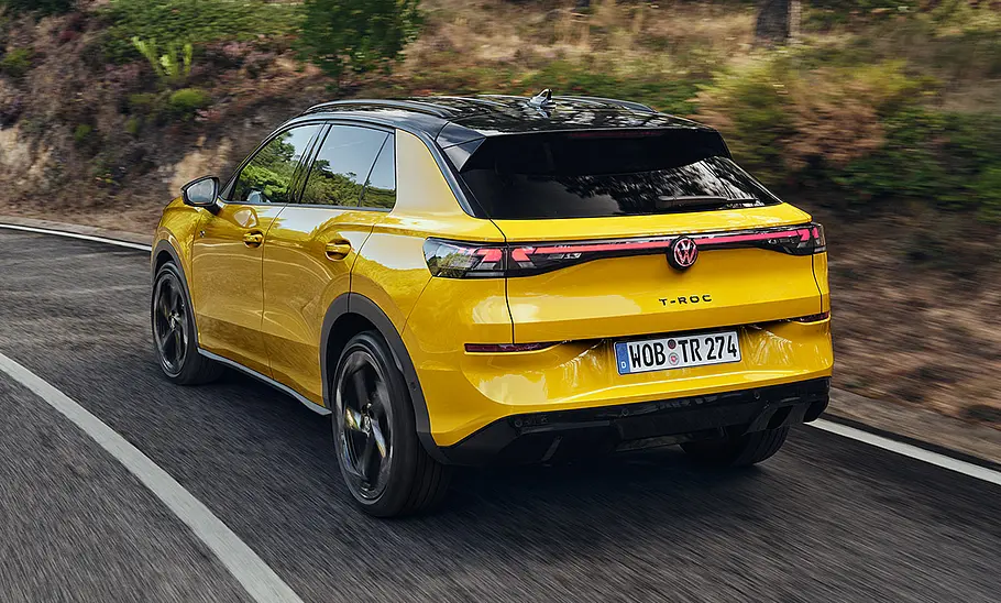 VW T-Roc Der VW T-Roc fährt durch eine Rechtskurve, fotografiert von schräg hinten.