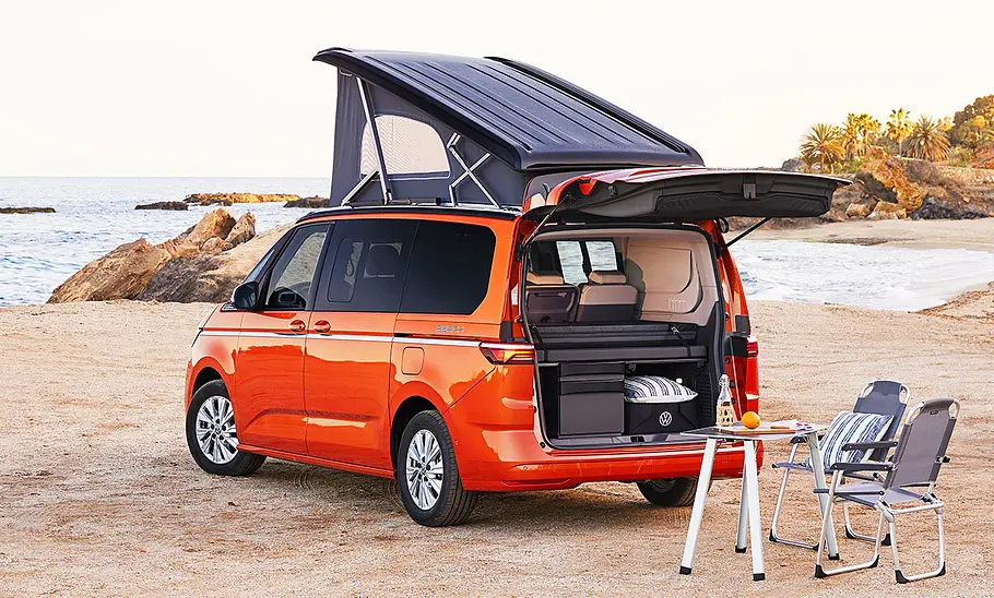 VW California (2024) Das Bild zeigt den VW California (2024) mit offenem Aufstelldach und geöffneter Heckklappe von schräg hinten links.