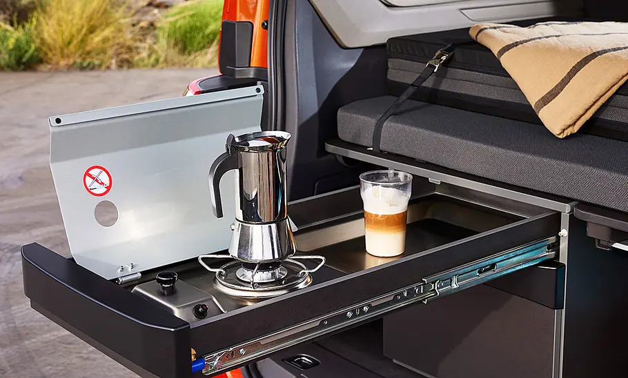 VW California (2024) Das Bild zeigt die ausgefahrene Küchenzeile im Heck des VW California Beach (2024) bei geöffneter Heckklappe.