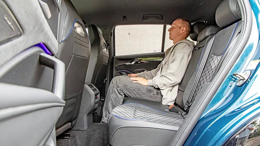 Toyota RAV4 und VW Tiguan im Vergleich Ein Mann in grauem Kapuzenpullover sitzt auf der Rückbank des VW Tiguan. Die hintere Tür ist geöffnet.