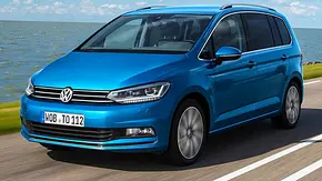 Der VW Touran (2015) fährt über eine Küstenstraße, von vorne links fotografiert. - Foto: VW