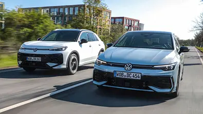 VW T-Roc und Golf fahren nebeneinander auf einer Straße, von vorne fotografiert. - Foto: VW