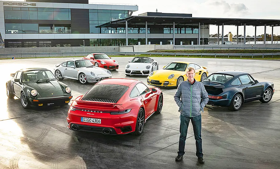 Walter Röhrl stehend vor Porsche-Modellen.