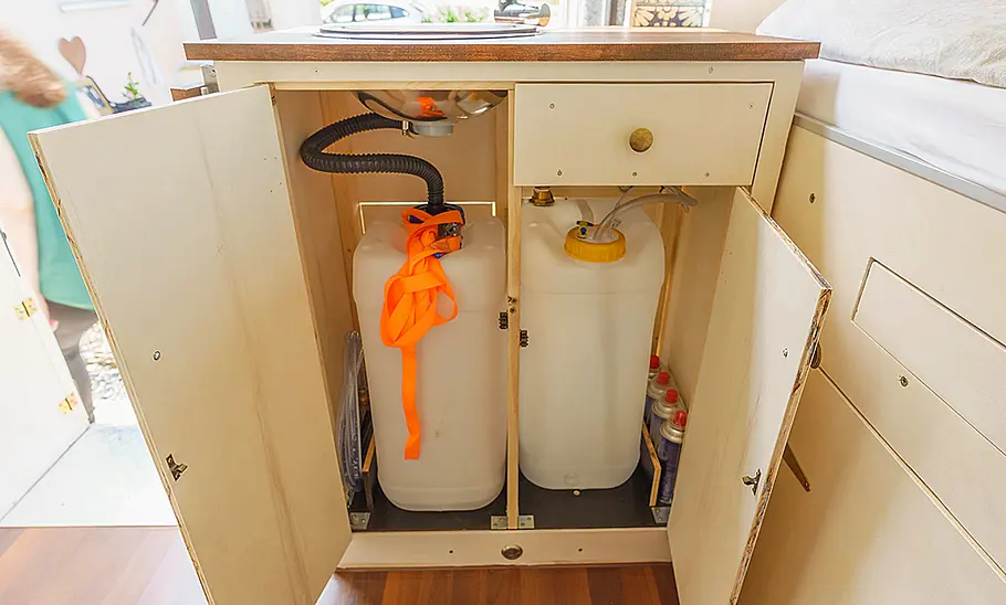 Das Bild zeigt einen Abwassertank (links) und einen Frischwassertank (rechts) in der Küchenzeile eines selbstausgebauten Wohnmobils.