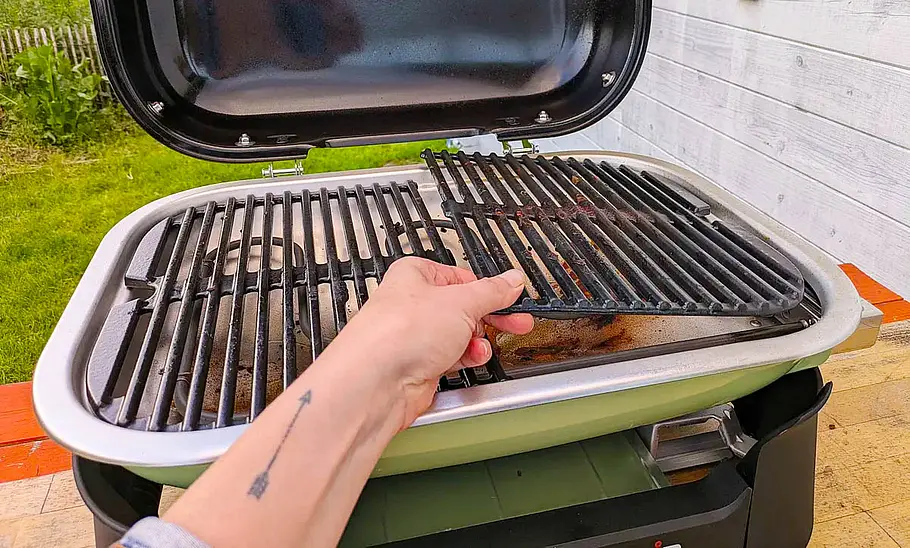 Weber Elektro-Tischgrill Lumin Eine Hälfte des Rostes des Weber Elektro-Tischgrill Lumin wird von einer Hand vom Grill genommen.