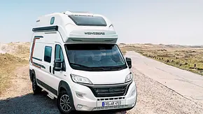 Die Außenaufnahme zeigt den Weinsberg Carabus 600 MQH von schräg vorne vor einem Strand. - Foto: Weinsberg