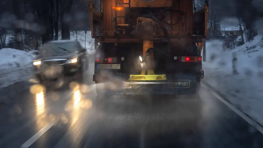 Streufahrzeug im Einsatz auf Landstraße mit Gegenverkehr, fotografiert von hinten.
